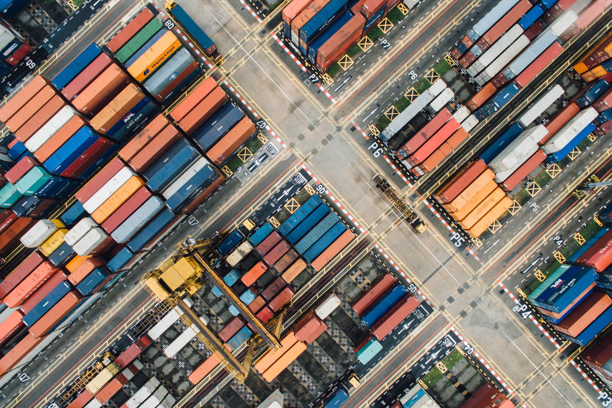 Photograph of a container storage facility with cranes and trucks moving and shipping them around